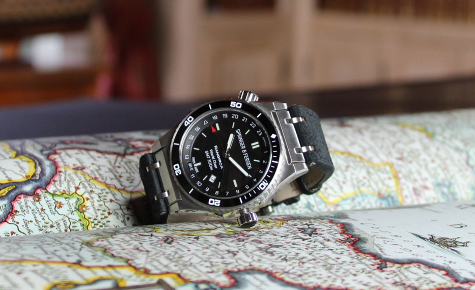 Inspired by travel: Springer & Fersen's Rangiroa World Diver watch in Deep-sea Blue laying on a map with all the globe-trotter's attributs: camera, hat and passeport. life is a journey, welcome on board!